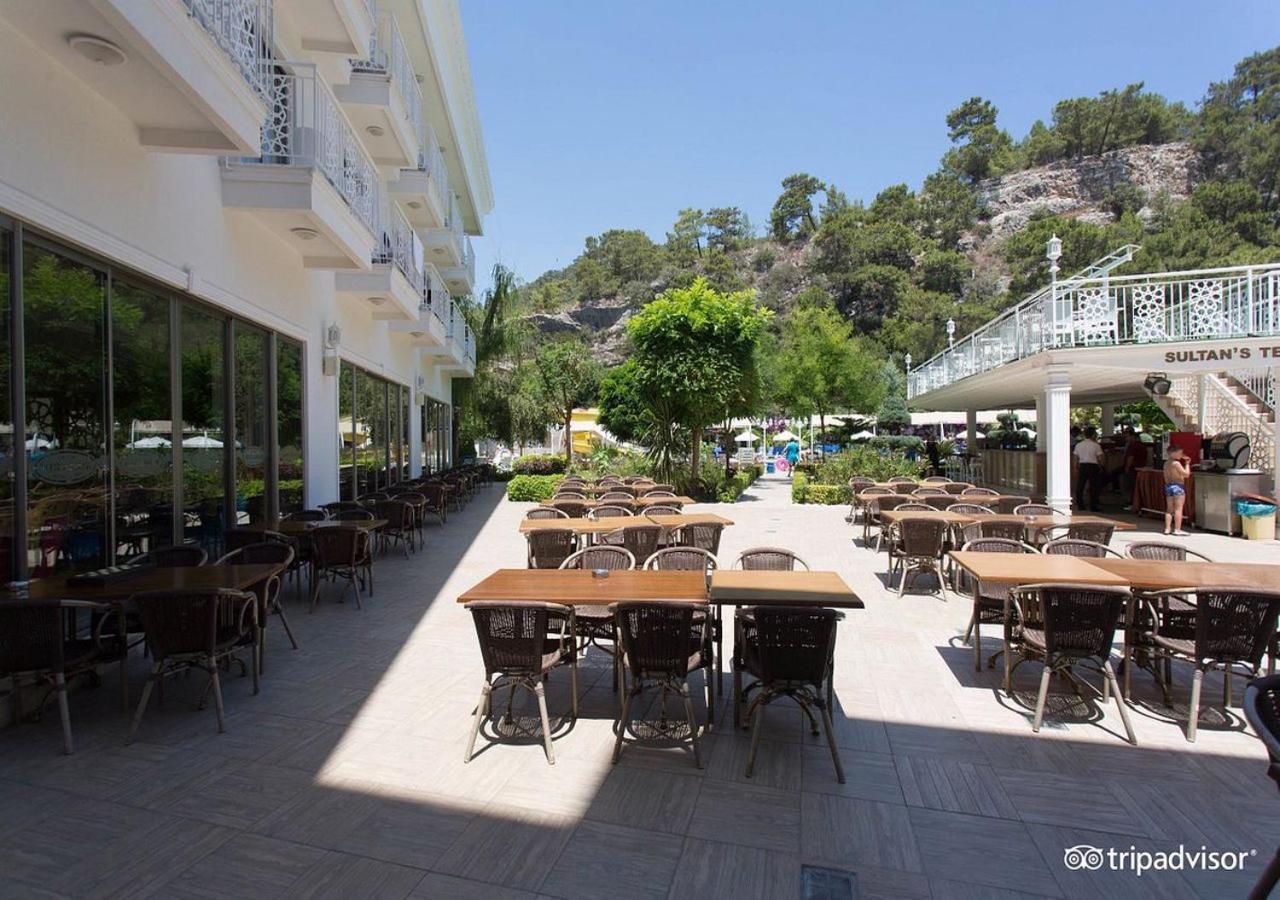 Miramor Hotel & Spa Анталья Экстерьер фото The photo shows an outdoor dining area, likely at a restaurant or cafe. There are several tables with chairs arranged neatly on the paved ground, and some greenery, such as trees and plants, is visible in the background. The setting appears bright an