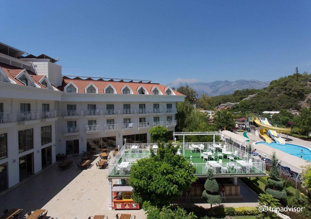 Miramor Hotel & Spa Анталья Экстерьер фото The photo shows a hotel or resort facility with a well-maintained exterior. There is a large green area with grass and some trees, likely intended for relaxation or recreational activities. In the background, there are water slides suggesting an amus